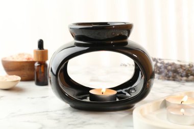 Aroma lambası, yanan mumlar, beyaz mermer masa üzerinde deniz tuzu ve temel yağ, yakın plan.