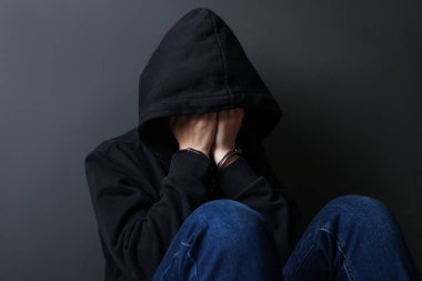 Metal kelepçeli bir kadın ve gri duvarın yanında elleri olan kapüşonlu bir kadın.