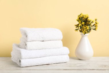 Beyaz havlu yığını ve çiçekler açık ahşap masa üzerinde sarı arka planda