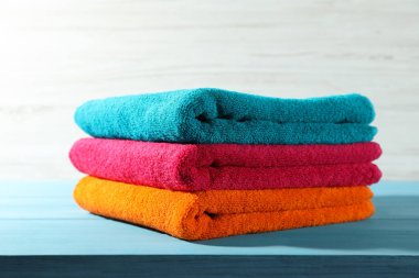 Mavi ahşap masadaki renkli temiz havlular beyaz arka plana karşı, yakın plan.