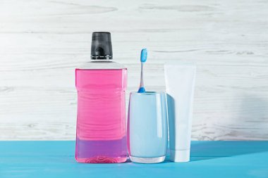 Ağız gargarası, diş macunu ve diş fırçası mavi ahşap masada beyaz arka planda. Ağız temizliği.