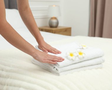 Kadın beyaz havlu yığını ve Plumeria çiçeklerini yatağın içine koyuyor, yakın plan.