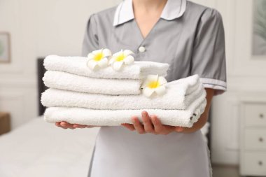 Otel odasında beyaz havlu yığınıyla oda hizmetçisi ve tesisat çiçekleri, yakın plan.