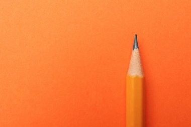 Turuncu arka planda keskin bir grafit kalem, üst manzara. Metin için boşluk