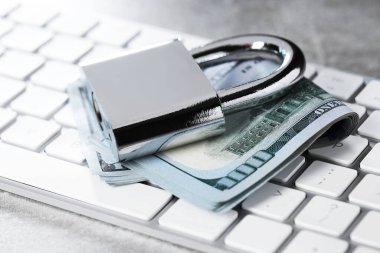 Siber güvenlik. Metal asma kilit, dolar banknotları ve gri masadaki bilgisayar klavyesi, yakın plan.