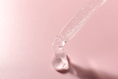 Pembe arka planda pipetten kozmetik ürünler damlatıyor, yakın plan. Metin için boşluk