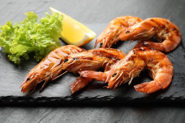 Siyah masada limonlu ve marullu ızgara karides, yakın plan. Lezzetli deniz ürünleri yemeği.