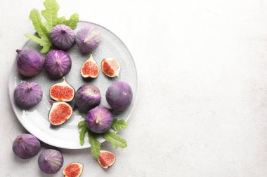 Taze incir ve yeşil yapraklar gri desenli masada, düz yerde. Metin için boşluk