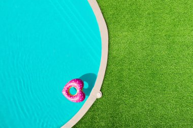 Kalp şeklinde şişirilebilir halka yüzme havuzunda yüzüyor yeşil çimlerle çevrili, üst manzara