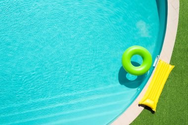 Yeşil çimlerle çevrili yüzme havuzunda yüzen şişme halka.