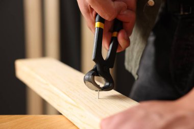 Kapalı alanda kıskaçlarla tahta çiviyi söken adam, yakın plan.