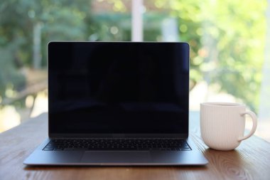 Laptop ve fincanı ahşap masada, bulanık yeşil arka planda, yakın plan. Tasarım için model