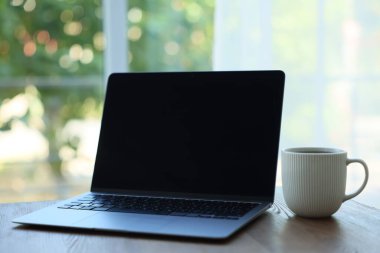 Laptop ve fincanı ahşap masada, bulanık yeşil arka planda, yakın plan. Tasarım için model