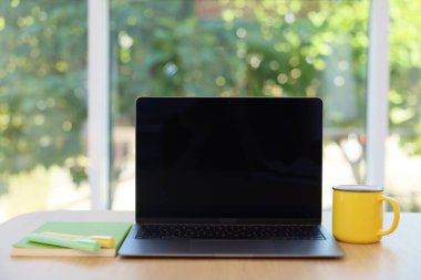 Laptop 'u, kırtasiyeyi ve kupayı açık bırak. Bulanık yeşil arka plan, yakın plan. Tasarım için model