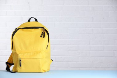 Sarı sırt çantası açık mavi masada beyaz tuğla duvara karşı. Metin için boşluk