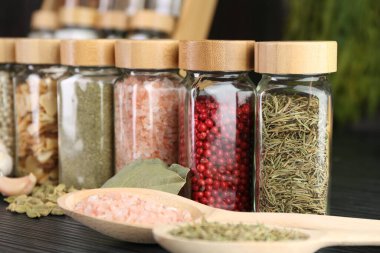 Gri ahşap masada farklı baharatlar ve cam kavanozlar, yakın plan.