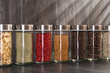 Gri ahşap masada cam kavanozlarda farklı baharatlar, yakın plan.