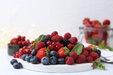 Beyaz fayanslı masada farklı olgun meyve ve nane yaprakları, yakın plan.