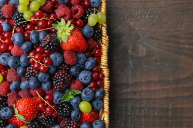 Farklı olgun böğürtlen ve nane yaprakları hasır sepetin içinde ahşap masanın üstünde, üst manzara. Metin için boşluk