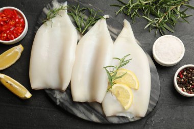 Limon dilimli pişmemiş mürekkep balıkları, biberiye ve baharatlar siyah masada, düz yerde.