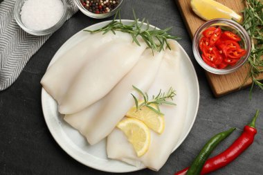 Limon dilimli pişmemiş mürekkep balıkları, biberiye ve baharatlar siyah masada, düz yerde.