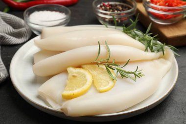 Limon dilimli pişmemiş mürekkep balıkları, biberiye ve baharatlar siyah masada, yakın plan.