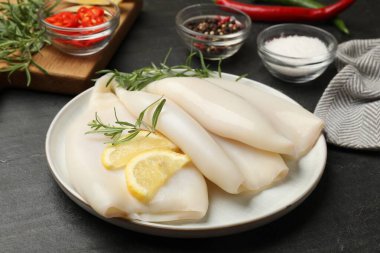 Limon dilimli pişmemiş mürekkep balıkları, biberiye ve baharatlar siyah masada, yakın plan.