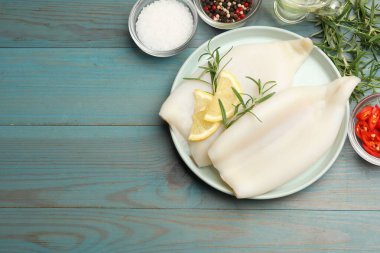 Limon dilimli pişmemiş mürekkep balıkları, biberiye ve baharatlar mavi ahşap masada, düz yerde. Metin için boşluk