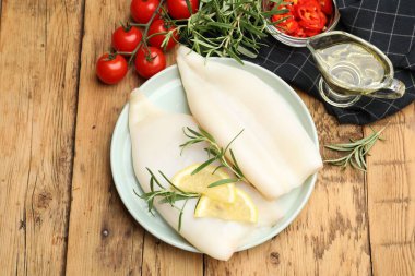 Limon dilimli pişmemiş mürekkep balıkları, ahşap masada biberiye ve baharatlar.