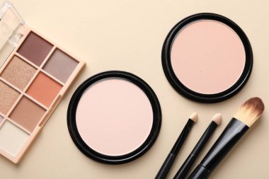 Göz falı paleti, yüz pudrası ve bej arka planda makyaj fırçaları, düz yatış