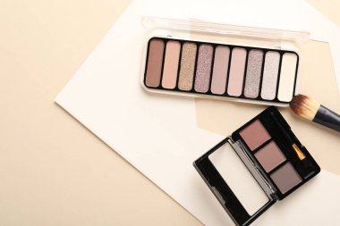 Renkli göz falı paletleri ve bej arka planda makyaj fırçası, düz yatış. Metin için boşluk