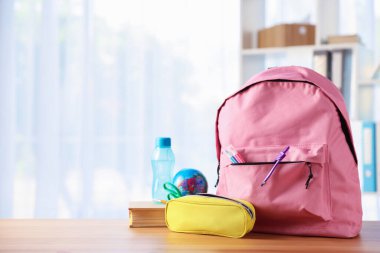 Sırt çantası, farklı kırtasiye malzemeleri, sınıfta masanın üstünde kitap ve bir şişe su. Metin için boşluk