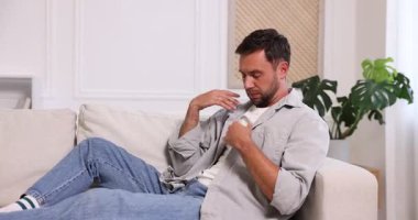 Sıcaktan muzdarip bir adam evdeki kanepede uzaktan kumandayla klimayı açıyor.