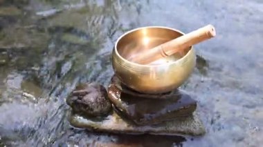 Nehirde taşın üzerinde tokmakla Tibet şarkı kasesi. Kamera yukarı hareket ediyor