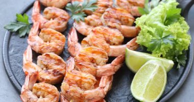 Lezzetli ızgara karidesli şişler, limon dilimleri, maydanoz ve marul gri masada dönüyor. Lezzetli deniz ürünleri yemeği.