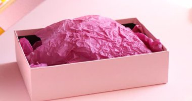 Kadın pembe arka planda güzel bir hediye kutusu açıyor, yakın plan.