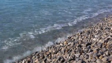Dalgalı deniz manzarası ve kumsaldaki çakıl taşları.