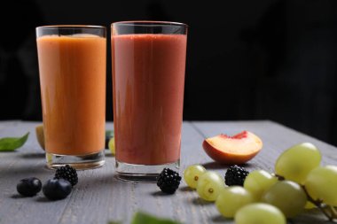 Gri ahşap masadaki farklı lezzetli meyve suları ve malzemeler koyu arka planda.