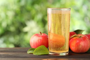 Cam, elma ve yeşil yapraklı nefis elma şarabı dışarıda ahşap masada, metin için yer var.