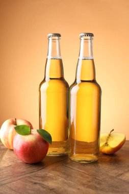 Cam şişelerde lezzetli elma şarabı ve ahşap masada portakal eğimli arka planda elmalar.