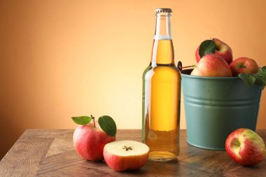 Cam şişede nefis elma şarabı ve portakal renkli arka planda ahşap masada elmalar. Metin için boşluk