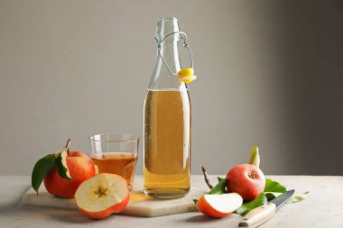 Şişede nefis elma şarabı, cam ve elmalar gri masada, arka planda ışığa karşı.