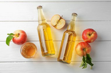 Cam şişelerde nefis elma şarabı ve beyaz ahşap masada elmalar.