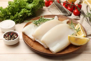 Hafif ahşap masa üzerinde ürünleri ve baharatları olan çiğ mürekkep balıkları, yakın plan.