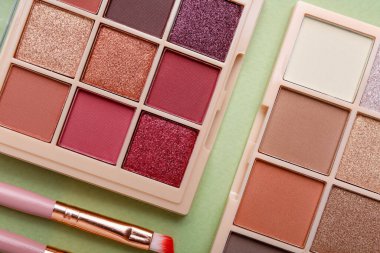 Renkli göz falı paletleri ve yeşil arka planda makyaj fırçası.