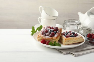 Böğürtlenli poğaça, pudra şekeri ve beyaz ahşap masada nane şekeri, metin için yer var.