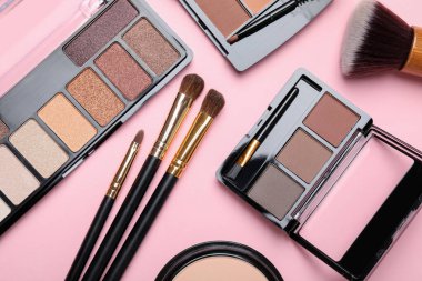 Renkli göz falı paletleri ve pembe arka planda makyaj fırçaları olan düz bir kompozisyon.