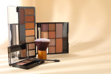 Renkli göz farı paletleri, makyaj aplikatörü ve gölgeli bej arka planda fırça, yakın plan. Metin için boşluk