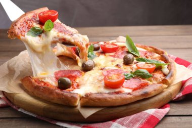Taking piece of delicious pizza with cheese, salami, tomatoes and olives at wooden table, closeup