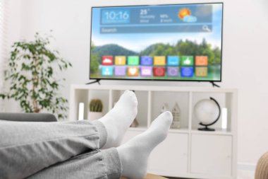 Evde televizyon izleyen bir adam, yakın çekim. Görünürde simge ve bilgi içeren menü